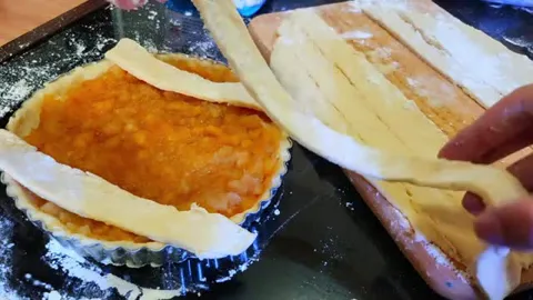 Hands arranging pastry strips over a filled pie case on a work surface.
