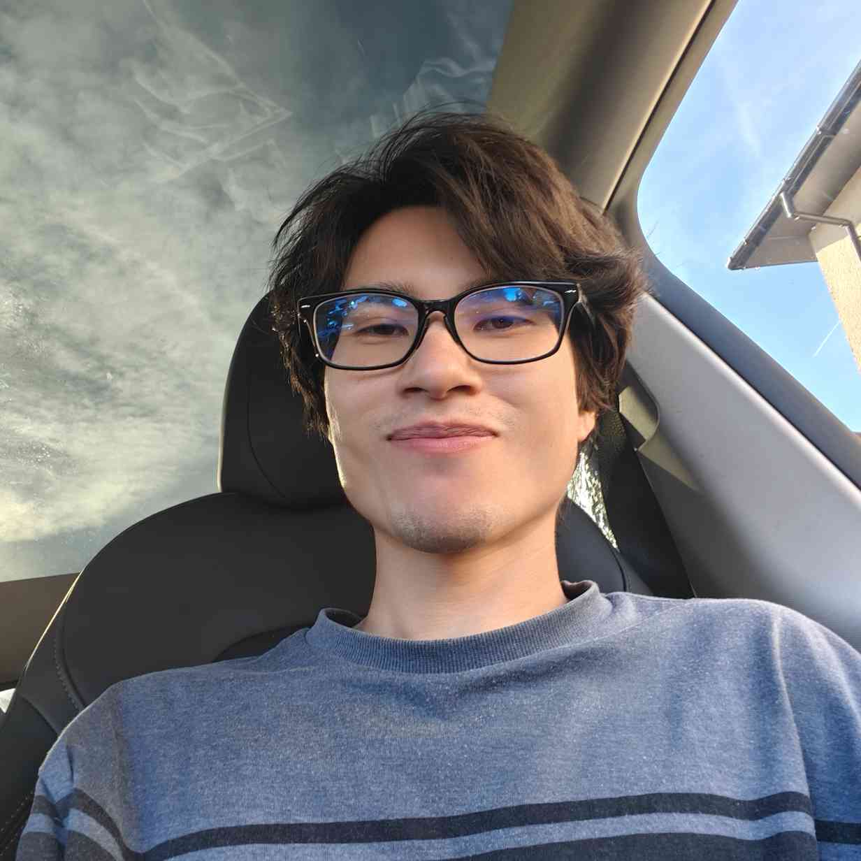 Account-posted portrait of a person wearing glasses and a blue jumper inside a car