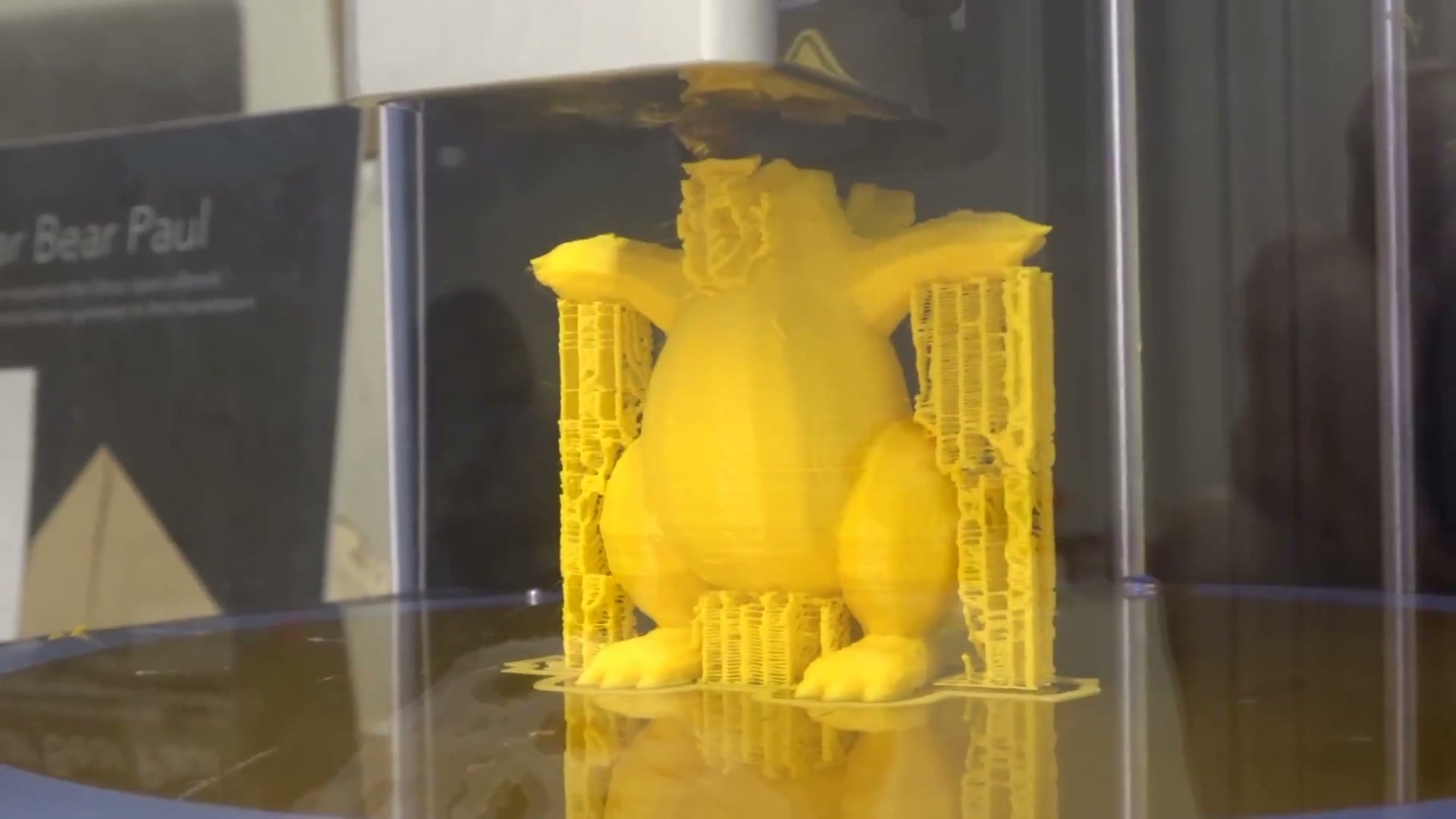 A yellow model surrounded by a thin support lattice inside a glass display.