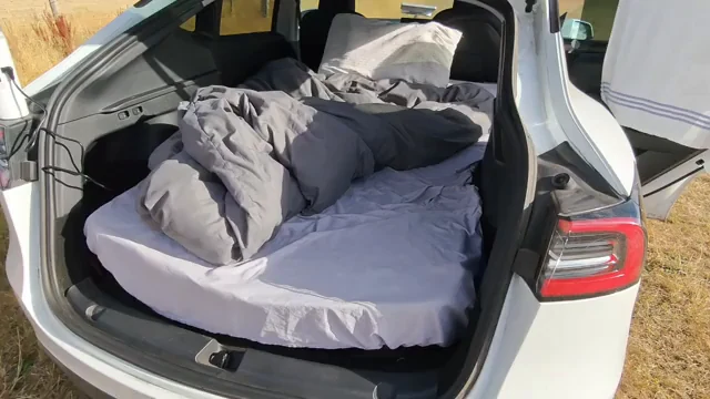 Open rear hatch with a mattress, pillows, sheets, and bedding arranged inside a white vehicle