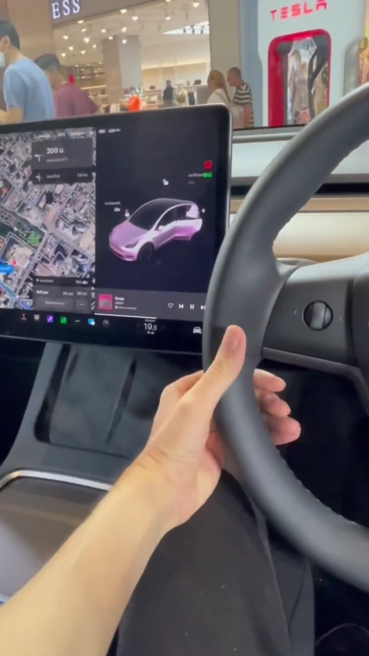 Right-hand-drive Tesla cabin with a central touchscreen showing a rendered vehicle and Tesla signage outside